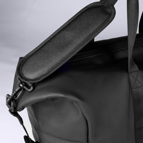 Teilansicht einer schwarzen Tasche mit Fokus auf die untere Seite und einen herunterhängenden, geöffneten Steckverschluss. Ein gepolsterter Schulterriemen und ein seitlicher Haken sind ebenfalls sichtbar