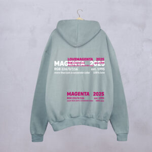 Der graublaue MAGENTA DEFINITION HOODIE hängt an einem Bügel an einer Betonwand. Auf der Rückseite steht in fettem Magenta und Weiß: MAGENTA 2025, LOVE MAGENTA und Farbcodes.