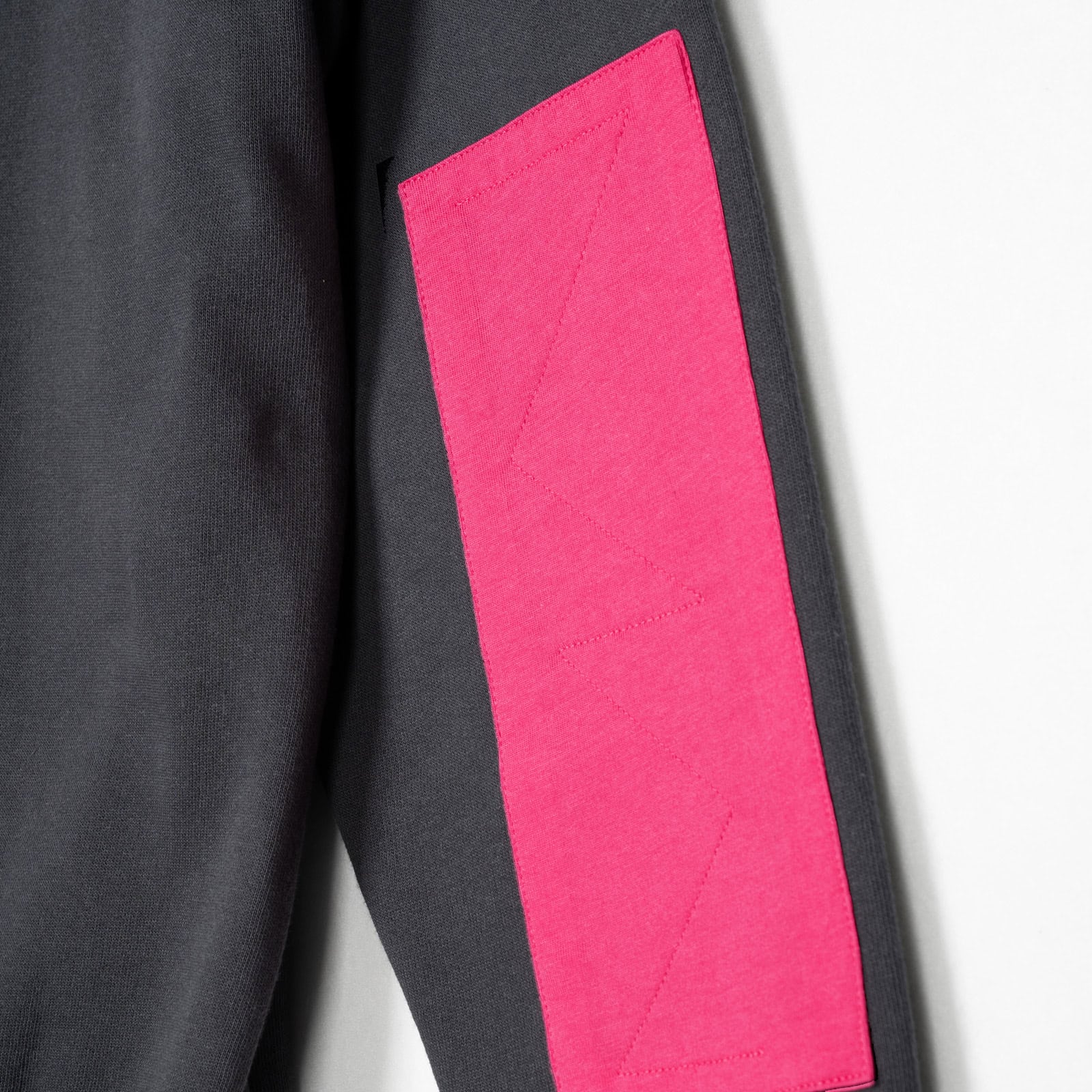 Eine Nahaufnahme des TEAM SWEATSHIRT-Ärmels in washed black zeigt einen großen, leuchtend magentafarbenen Aufnäher mit aufgestickten Mustern auf weißem Hintergrund.