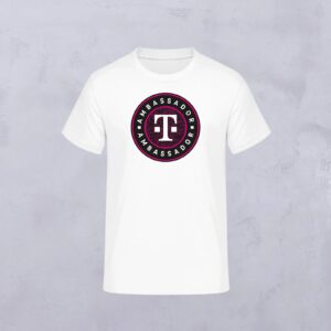 Das AMBASSADOR ROUND T-SHIRT WHITE zeigt ein kreisförmiges "AMBASSADOR"-Logo mit dem T-Logo in der Mitte auf einem weißen T-Shirt vor einem hellgrauen Hintergrund.