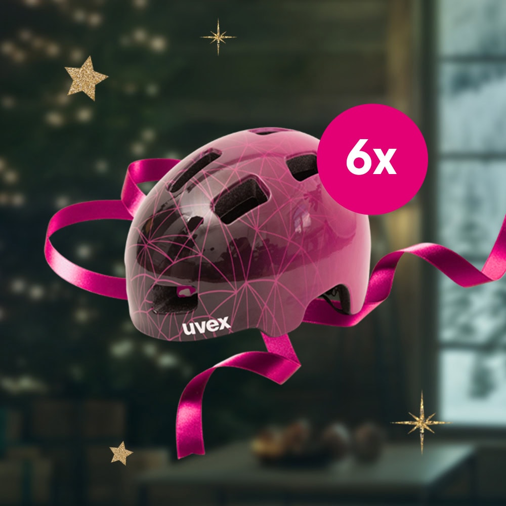 Ein magentafarbener Uvex-Fahrradhelm mit geometrischem Muster und Schleife, 6x magentafarbener Kreis, verschwommener Weihnachtsbaum und Sterne im Hintergrund.