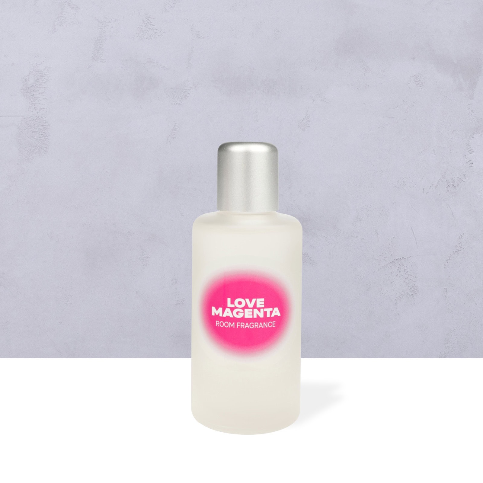 LOVE MAGENTA ROOM SCENT in einem Milchglasflakon mit silberner Kappe auf weißer Oberfläche, dahinter hellgrauer, strukturierter Hintergrund.