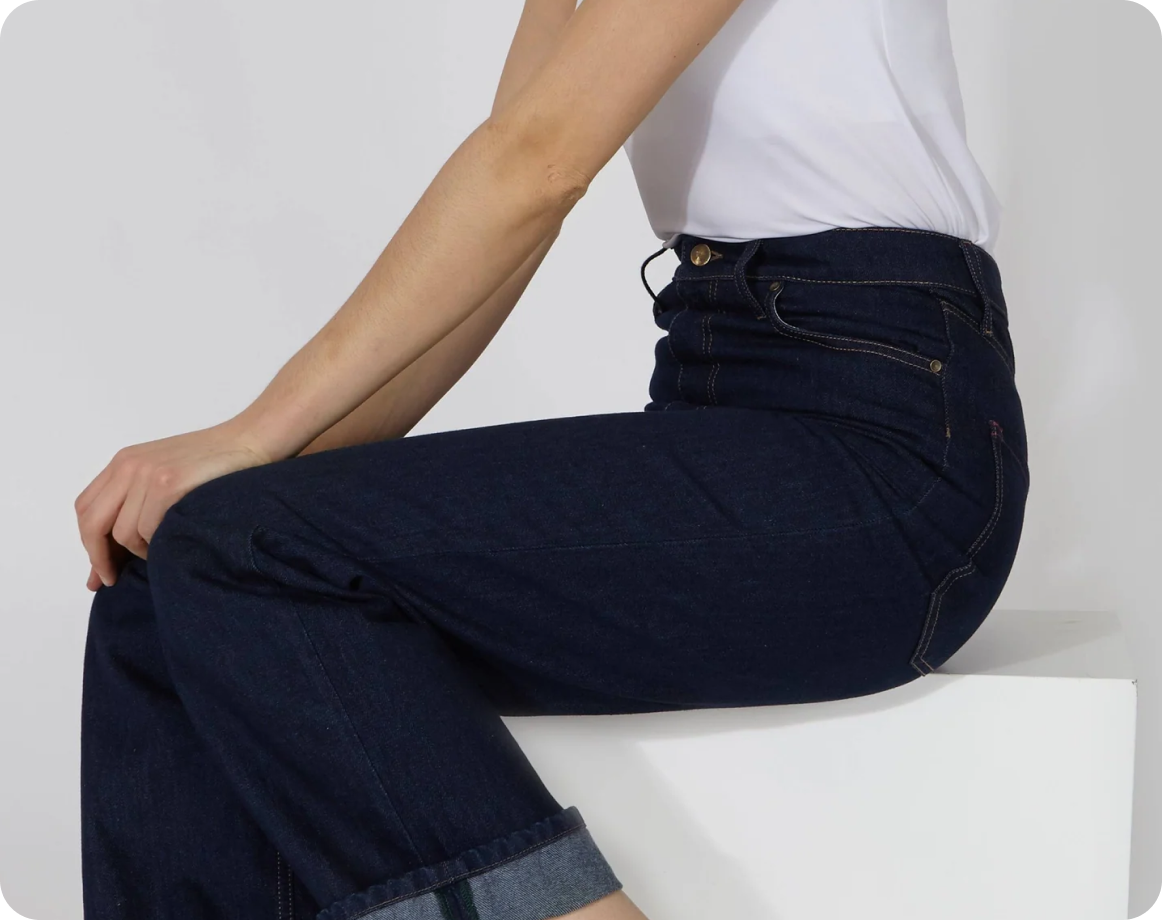 Eine Person in einem weißen kurzärmeligen Oberteil und dunkelblauen Jeans mit gelben Nähten sitzt auf einem weißen Block, passend zum Thema LOVE MAGENTA.