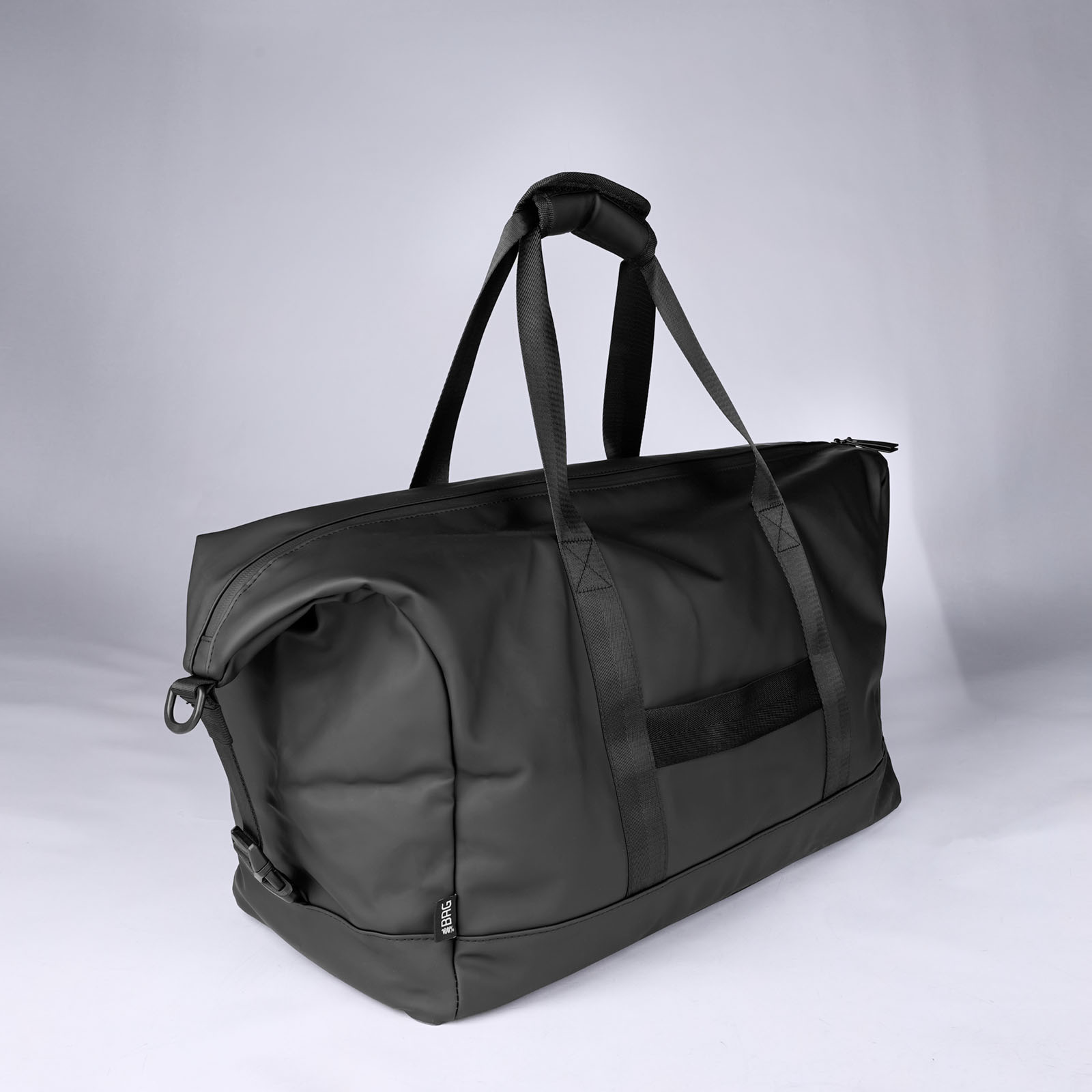 Auf einem schlichten hellgrauen Hintergrund ist eine schwarze Reisetasche mit zwei Tragegriffen und einem Schultergurt zu sehen. Die Tasche hat einen rechteckigen Boden und einen großen Reißverschluss.