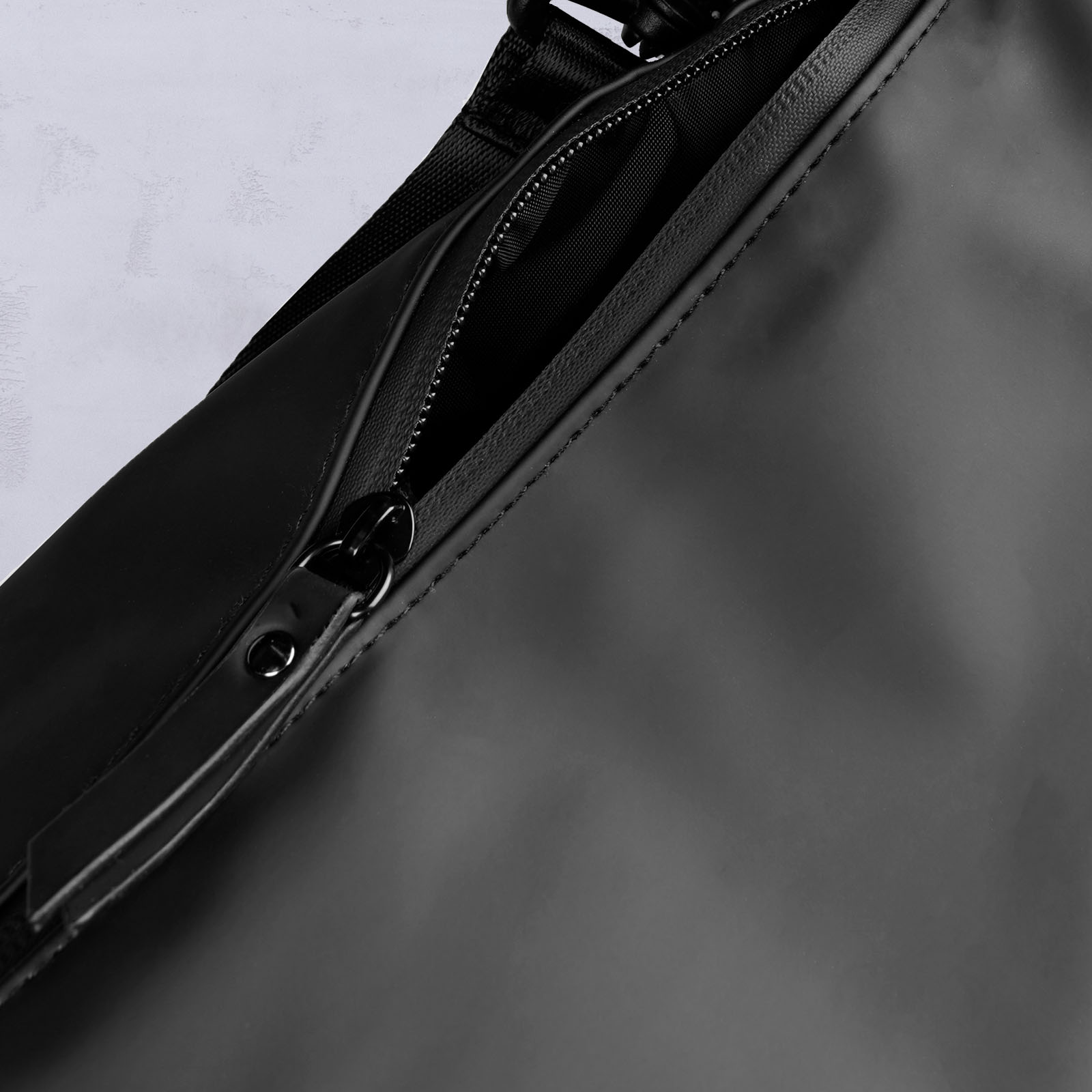 Nahaufnahme eines teilweise geöffneten schwarzen Reißverschlusses an einer glatten, mattschwarzen Tasche, die einen Blick auf die innere Netztasche freigibt.