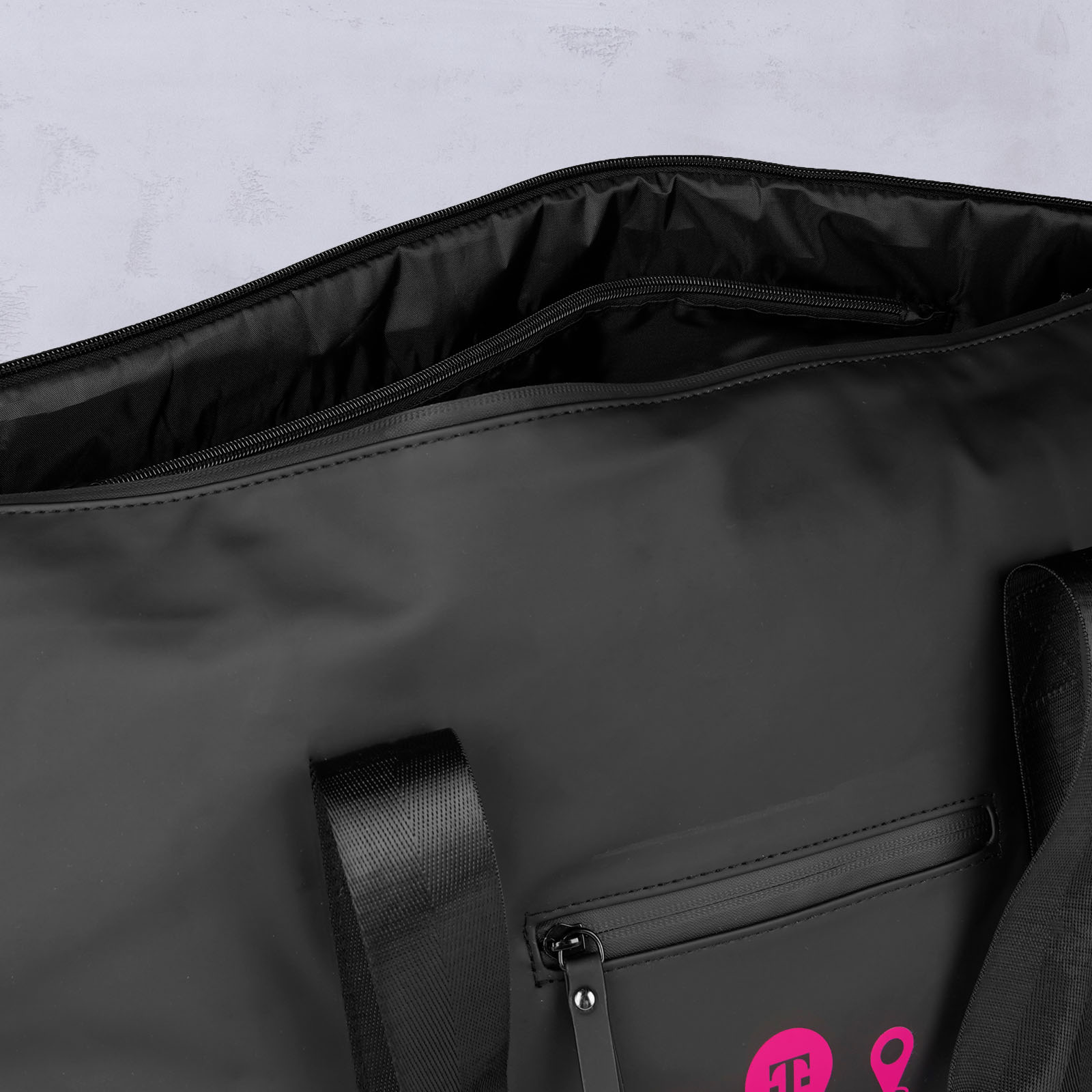 Eine Nahaufnahme einer schwarzen Tragetasche mit Reißverschluss, schwarzen Tragegriffen und einer kleinen Außentasche mit Reißverschluss. Auf der Vorderseite der Tasche sind rosa Motive abgebildet.