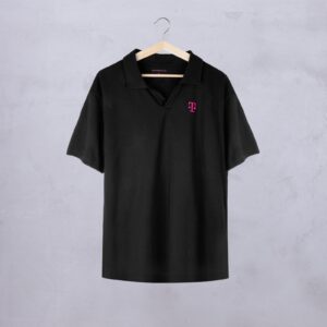Ein schwarzes Kurzarm-Poloshirt auf einem Holzkleiderbügel mit einem kleinen magentafarbenen T-Logo auf der linken Brust, das vor einer hellgrauen, strukturierten Wand hängt.