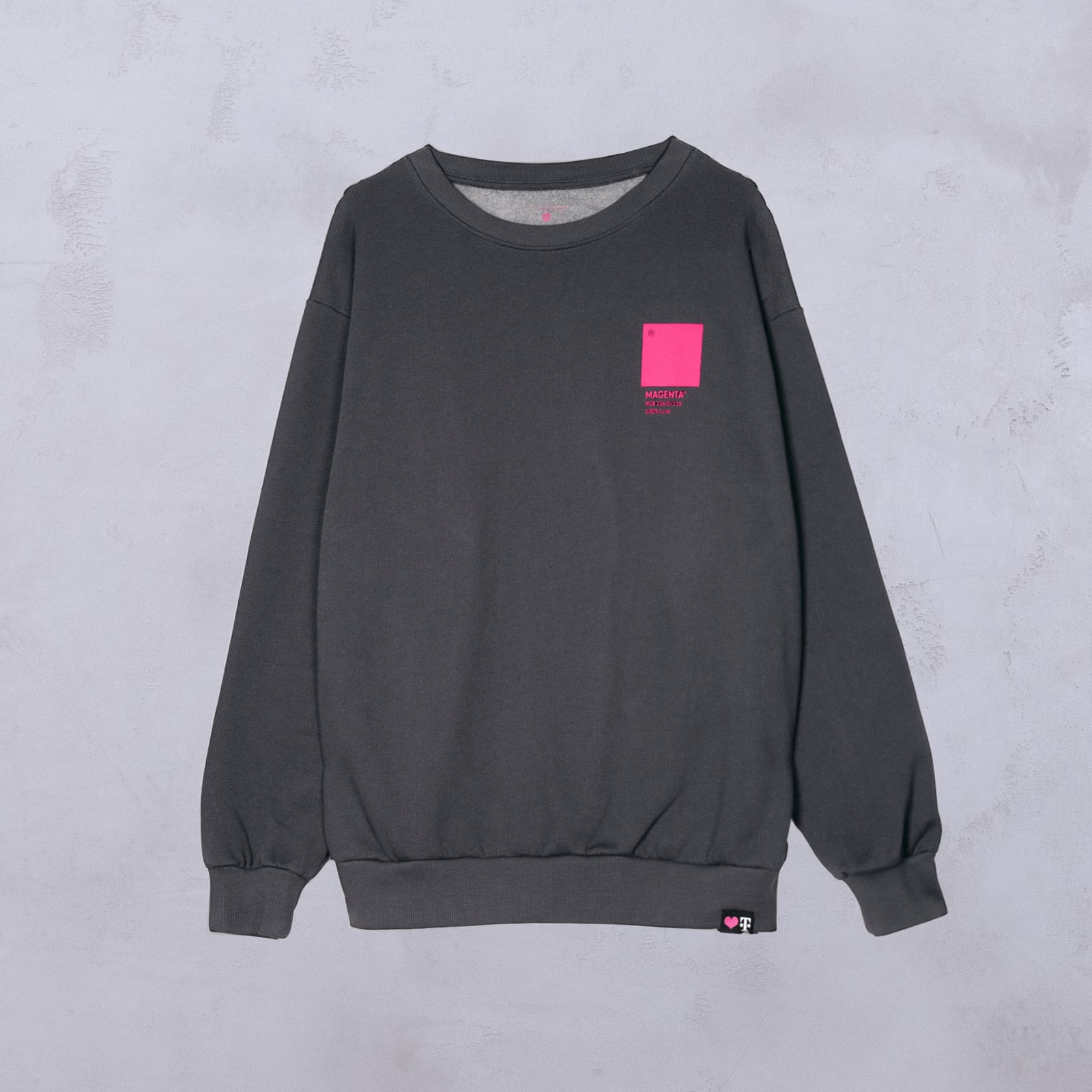Dunkelgraues Sweatshirt mit Rundhalsausschnitt, einem leuchtend pinkfarbenen Quadrat und kleiner Schrift auf der linken Brustseite. Das Sweatshirt hat lange Ärmel sowie gerippte Bündchen und einen gerippten Saum und wird vor einem hellgrauen, strukturierten Hintergrund gezeigt.