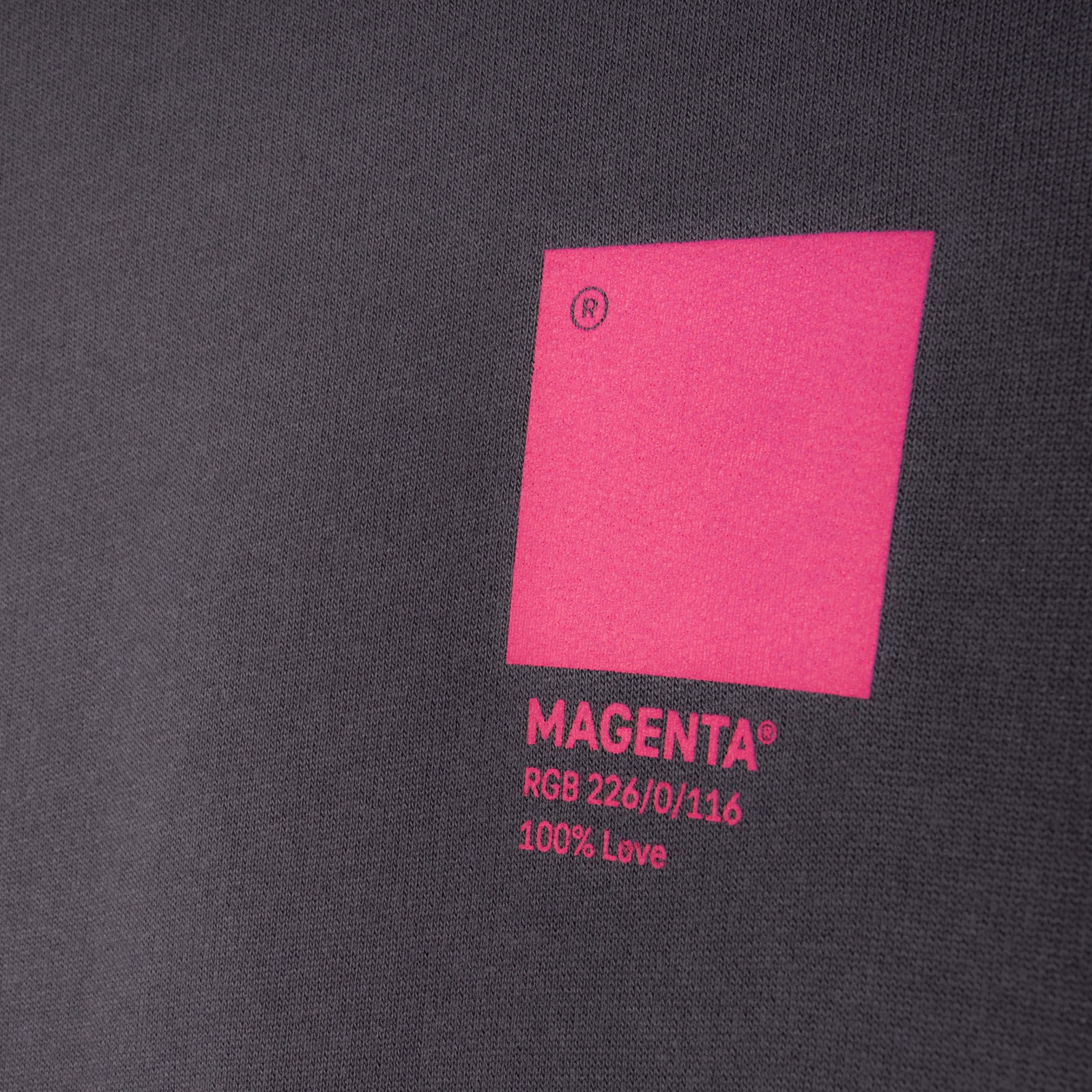 Ein magentafarbenes Quadrat mit dem darunter stehenden Text „MAGENTA, RGB 226/0/116, 100 % Love“ auf einem dunklen Stoffhintergrund.