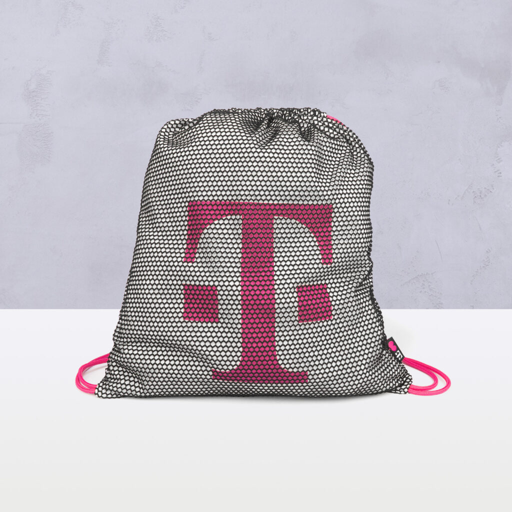 Ein Beutel mit Kordelzug, der ein schwarz-weißes Netzmuster aufweist und auf dessen Vorderseite ein großes rosa „T“-Logo vor einem hellgrauen Hintergrund zu sehen ist.