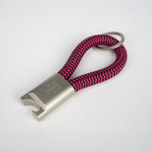 Ein silberner Flaschenöffner-Schlüsselanhänger mit einer rosa-schwarzen geflochtenen Schlaufe und einem Metallschlüsselring, dargestellt vor einem weißen Hintergrund.
