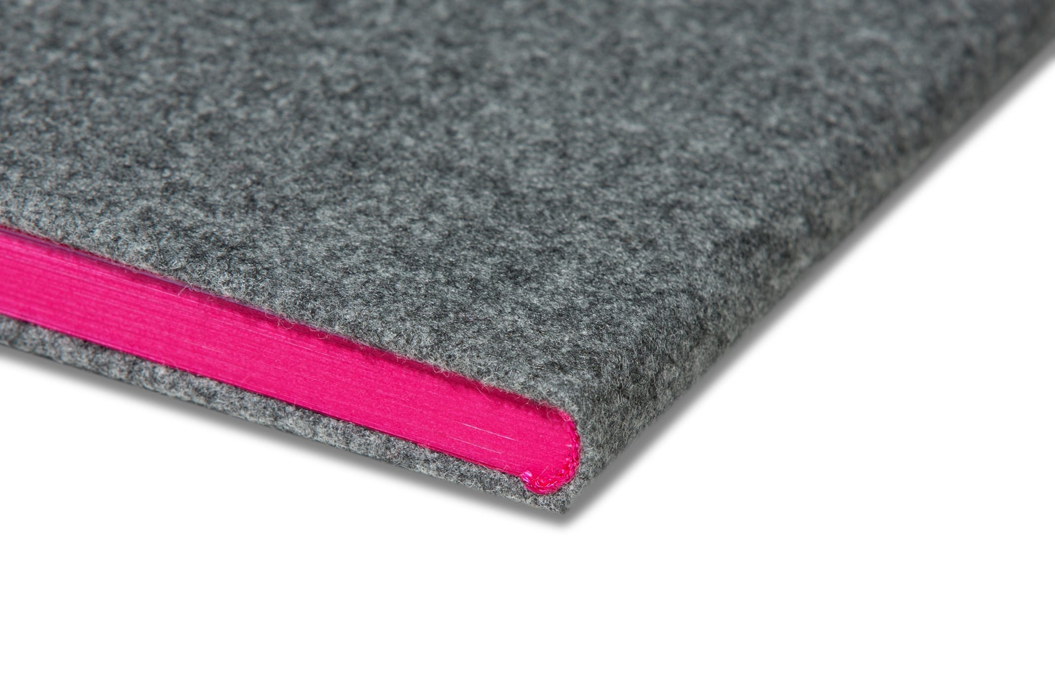 Eine Nahaufnahme eines geschlossenen Buches mit einem grauen Filzeinband und leuchtend pinkfarbenen Seitenrändern, fotografiert vor einem weißen Hintergrund.