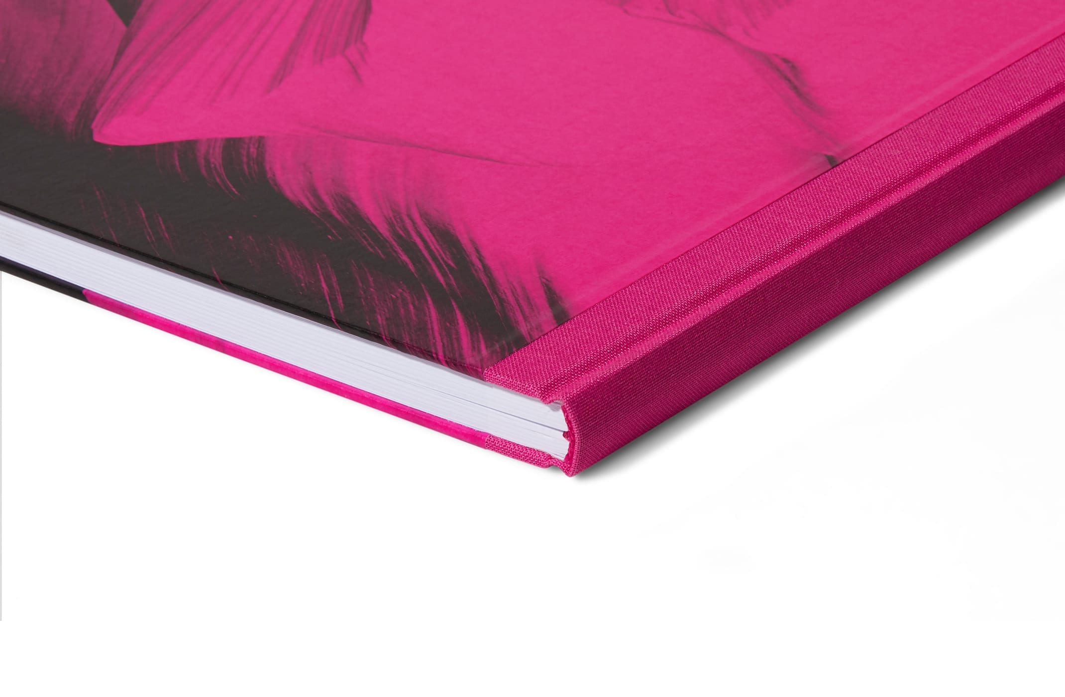 Eine Nahaufnahme der Ecke eines gebundenen Buches mit leuchtend pinkfarbenem Einband und Buchrücken, auf dem teilweise ein aufgedrucktes Motiv zu sehen ist. Das Buch liegt auf einer weißen Unterlage.