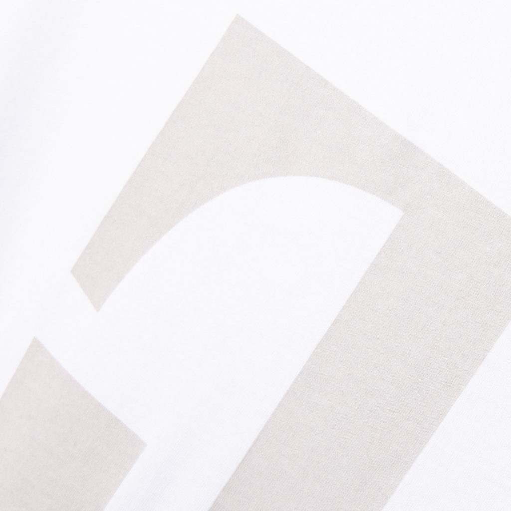 Nahaufnahme eines weißen Stoffes mit einem großen, hellgrauen geometrischen oder typografischen Muster, auf dem ein Teil einer geschwungenen und einer geraden Kante zu sehen ist.