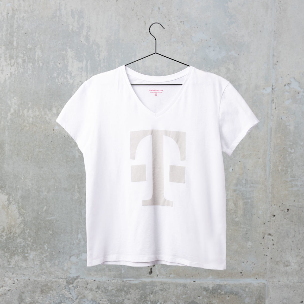 Ein weißes T-Shirt mit kurzen Ärmeln und einem großen hellgrauen T-Logo auf der Brust hängt an einem schwarzen Kleiderbügel vor einer strukturierten grauen Betonwand.