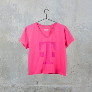 Ein rosa T-Shirt mit einem großen, magentafarbenen „T“-Logo auf der Vorderseite hängt an einem schwarzen Kleiderbügel vor einer grauen Betonwand.