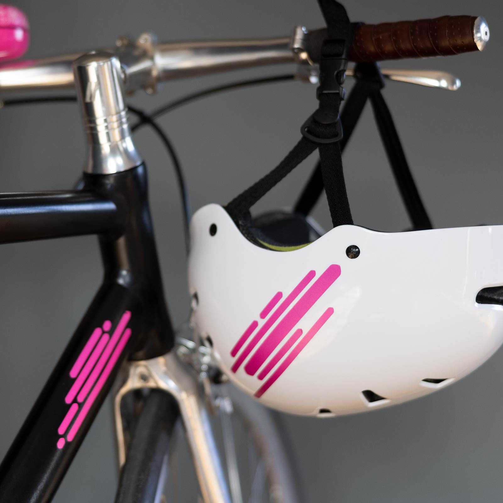 Nahaufnahme eines schwarzen Fahrrads mit rosa Details und eines weißen Helms mit passenden rosa Streifen, der am Lenker hängt.