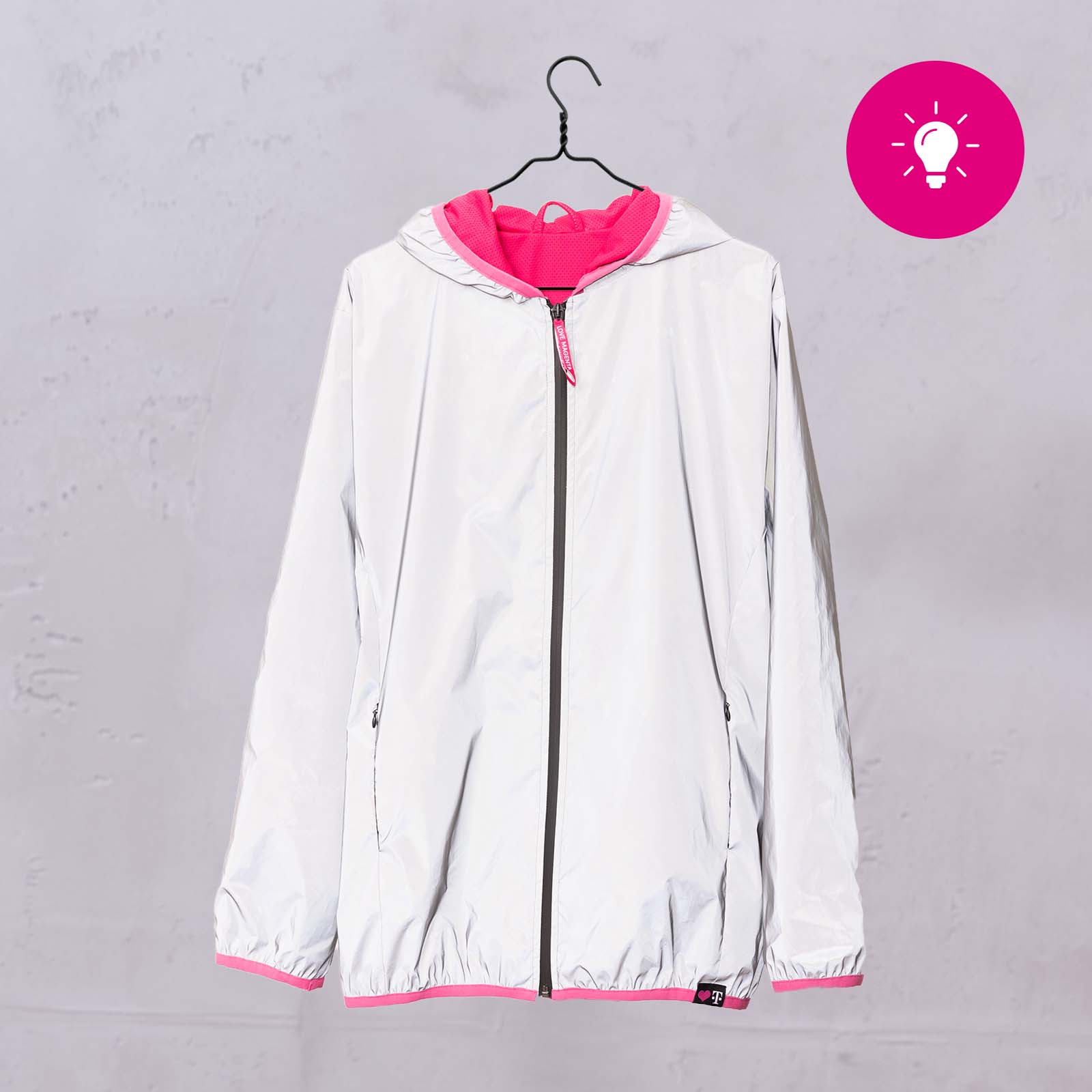 An einem schwarzen Kleiderbügel hängt eine weiße Jacke mit rosa Futter vor einer hellgrauen Wand. In der rechten oberen Ecke des Bildes ist ein rosa Symbol mit einer weißen Glühbirne zu sehen.