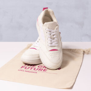 Zwei weiße Sneaker mit magentafarbenen Akzenten liegen auf einem cremefarbenen Beutel mit Kordelzug, auf dem in rosa Schrift „THE GREEN FUTURE“ und „LOVE MAGENTA“ steht. Die Sneaker sind stilvoll und sportlich und zeichnen sich durch ein minimalistisches Design aus.