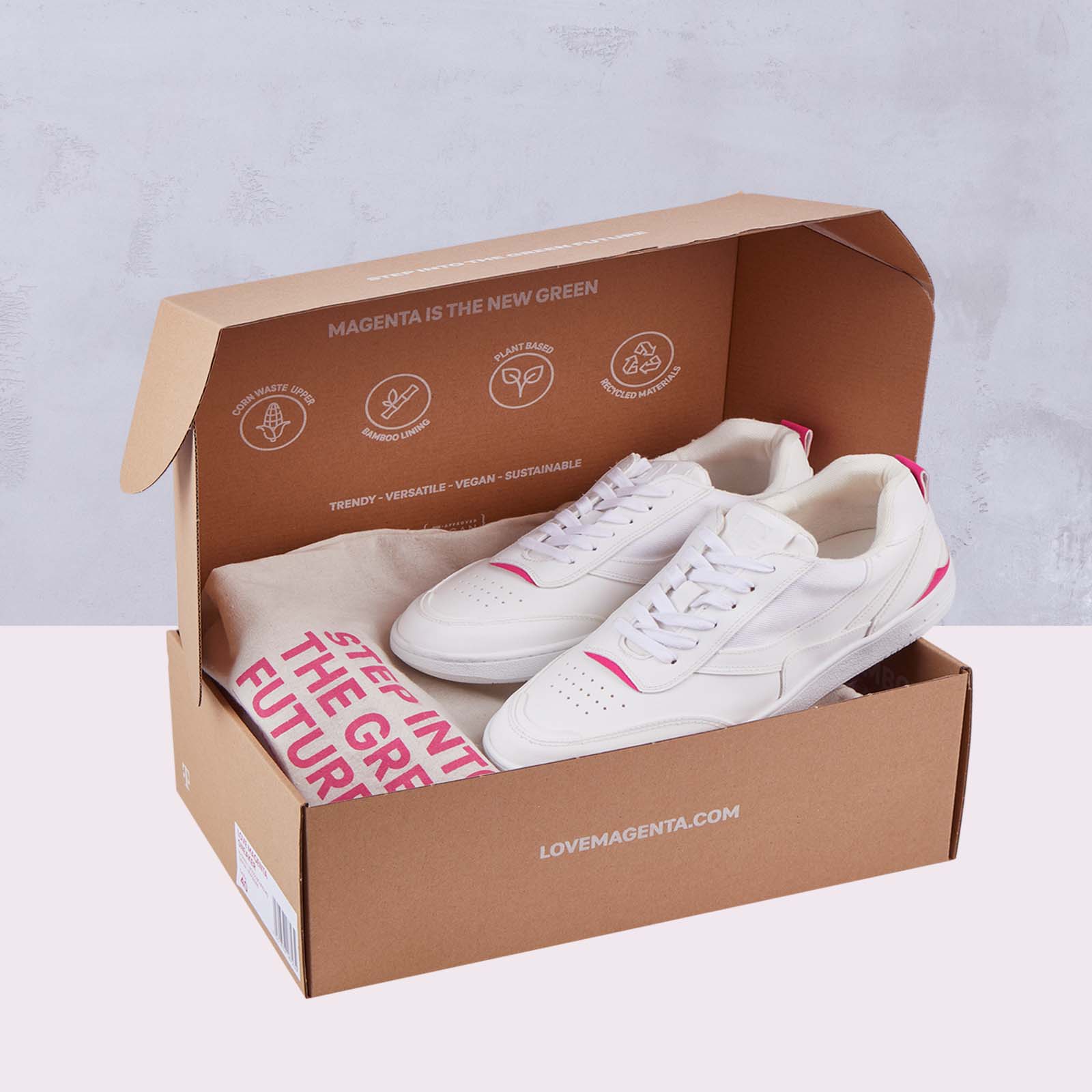 In einem offenen Karton liegt ein Paar weiße Sneaker mit rosa Akzenten. Auf dem Kartondeckel sind Symbole für Umweltfreundlichkeit und ein Text zu sehen. Außerdem befindet sich ein gefaltetes T-Shirt mit einer auffälligen rosa Aufschrift im Karton.