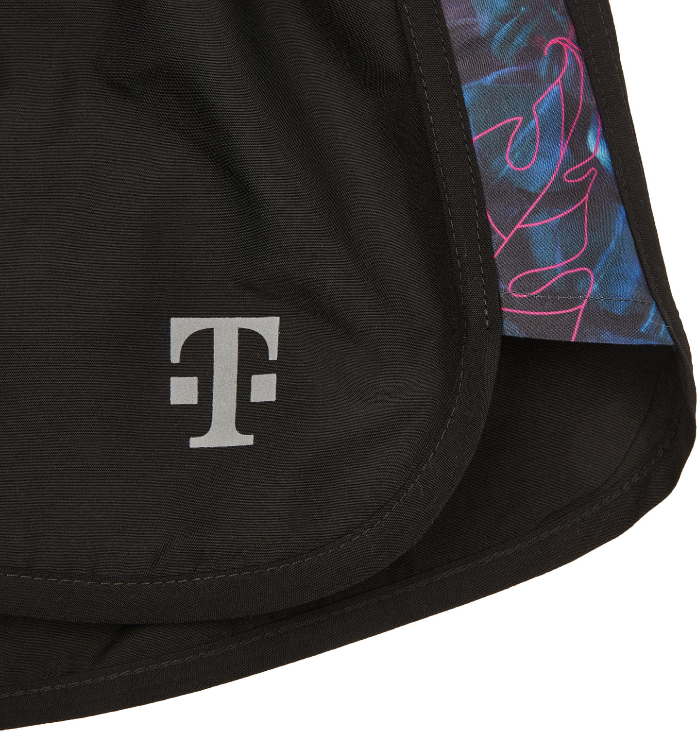 Nahaufnahme von schwarzen Sportshorts mit einem reflektierenden T-Logo und einem Seiteneinsatz mit einem abstrakten Muster in Blau und Rosa.