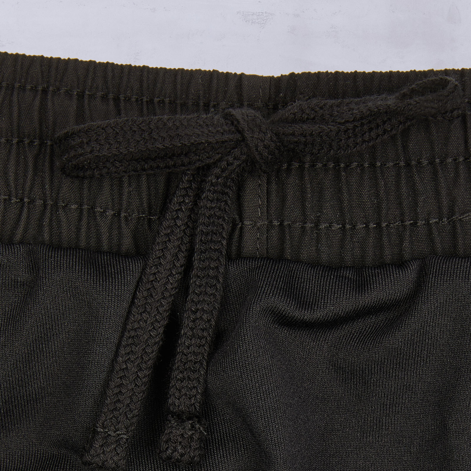 Nahaufnahme des Bunds einer schwarzen Hose mit Gummizug und einem schwarzen Kordelzug, der zu einer Schleife gebunden ist.