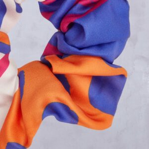 Eine Nahaufnahme eines Stoffes mit welliger Struktur, der auf hellgrauem Hintergrund kräftige orangefarbene, blaue, rosa und cremefarbene Bereiche aufweist.