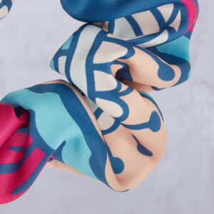 Ein Scrunchie aus Stoff mit einem farbenfrohen abstrakten Muster in Blau