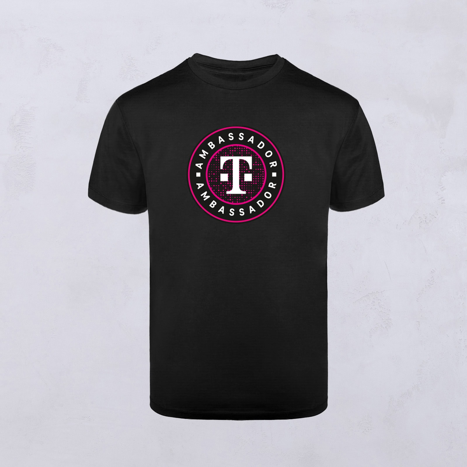 Schwarzes T-Shirt mit einem runden Logo in der Mitte. Das Logo zeigt ein weißes „T“ in einem kastanienbraunen Kreis, umrandet von dem Wort „AMBASSADOR“, das in weißen Buchstaben um den Rand herum wiederholt wird – ein Markenzeichen von Ambassador Designs.