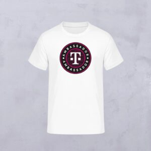 Weißes T-Shirt mit einem runden Logo in der Mitte. Das Logo trägt die Aufschrift „I AM AMBASSADOR“ um ein markantes Symbol herum, das wie eine abstrakte Figur oder ein Buchstabe aussieht, in den Farben Schwarz, Weiß und Rot – ein charakteristisches Detail, das vom LOVE MAGENTA Studio inspiriert ist. Der Hintergrund ist hellgrau.