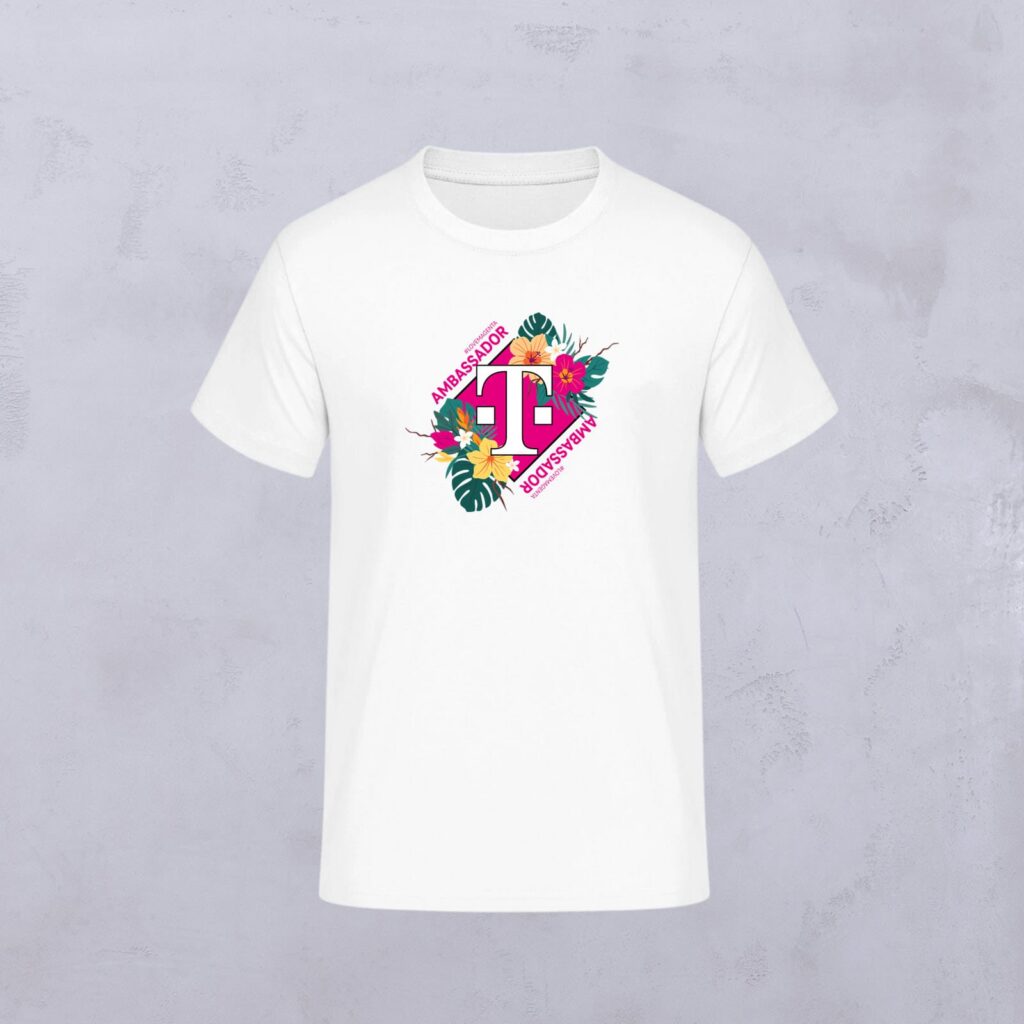 Weißes T-Shirt mit einem rosa geometrischen Logo in der Mitte, umgeben von bunten Blumen und grünen Blättern. Die Schriftzüge „Ambassadors“ und „Women Power“ umrahmen das Motiv und spiegeln den lebendigen Geist von LOVE MAGENTA Studio wider.