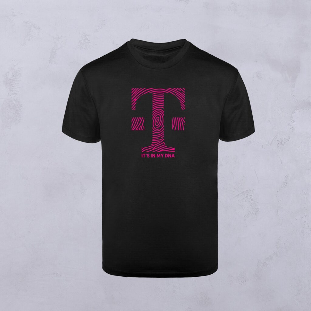 Ein schwarzes T-Shirt mit Euerem Motiv – einem großen magentafarbenen Buchstaben „T“ mit fingerabdruckartigen Linien – und dem Schriftzug „ITS IN MY DNA“ in kleinen magentafarbenen Buchstaben unterhalb des „T“.