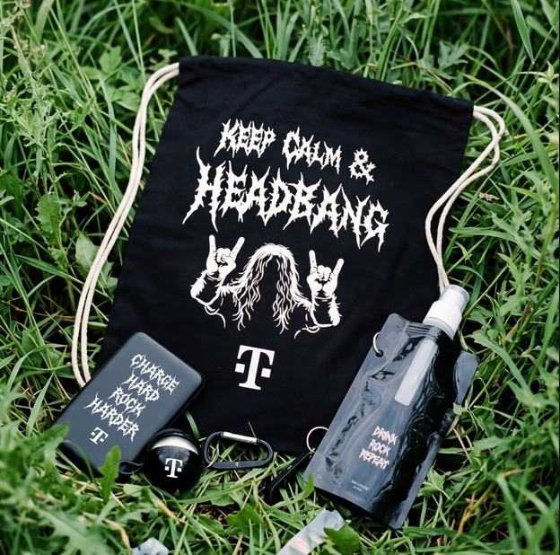 Auf dem grünen Rasen lagen ein schwarzer Beutel mit Kordelzug und der Aufschrift „Keep Calm & Headbang“, Ohrstöpsel und zwei schwarze Wasserflaschen. Die Gegenstände sind mit Schriftzügen und Motiven im Rock-Stil versehen.