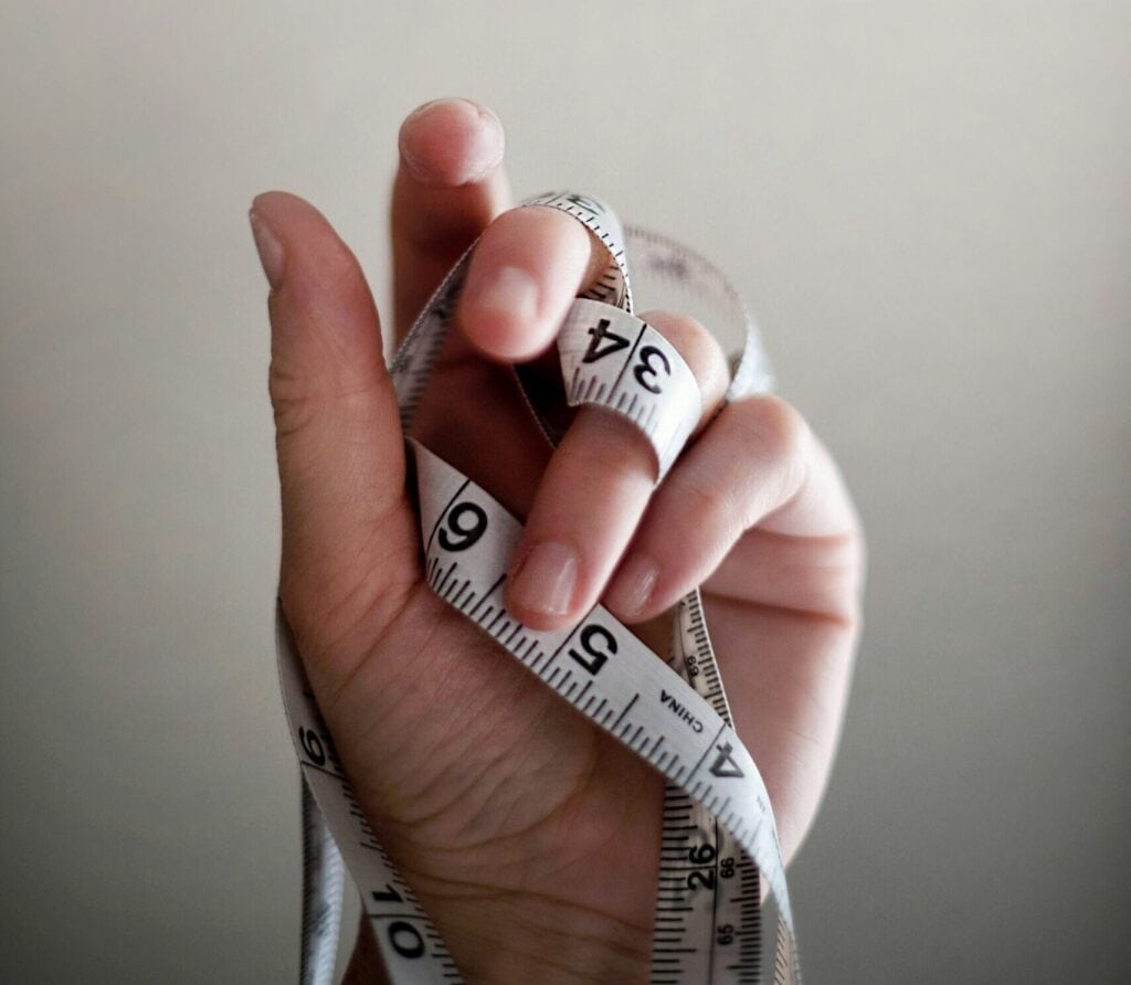 Eine Hand, die ein Maßband hält und es vor einem einfarbigen Hintergrund um ihre Finger wickelt.