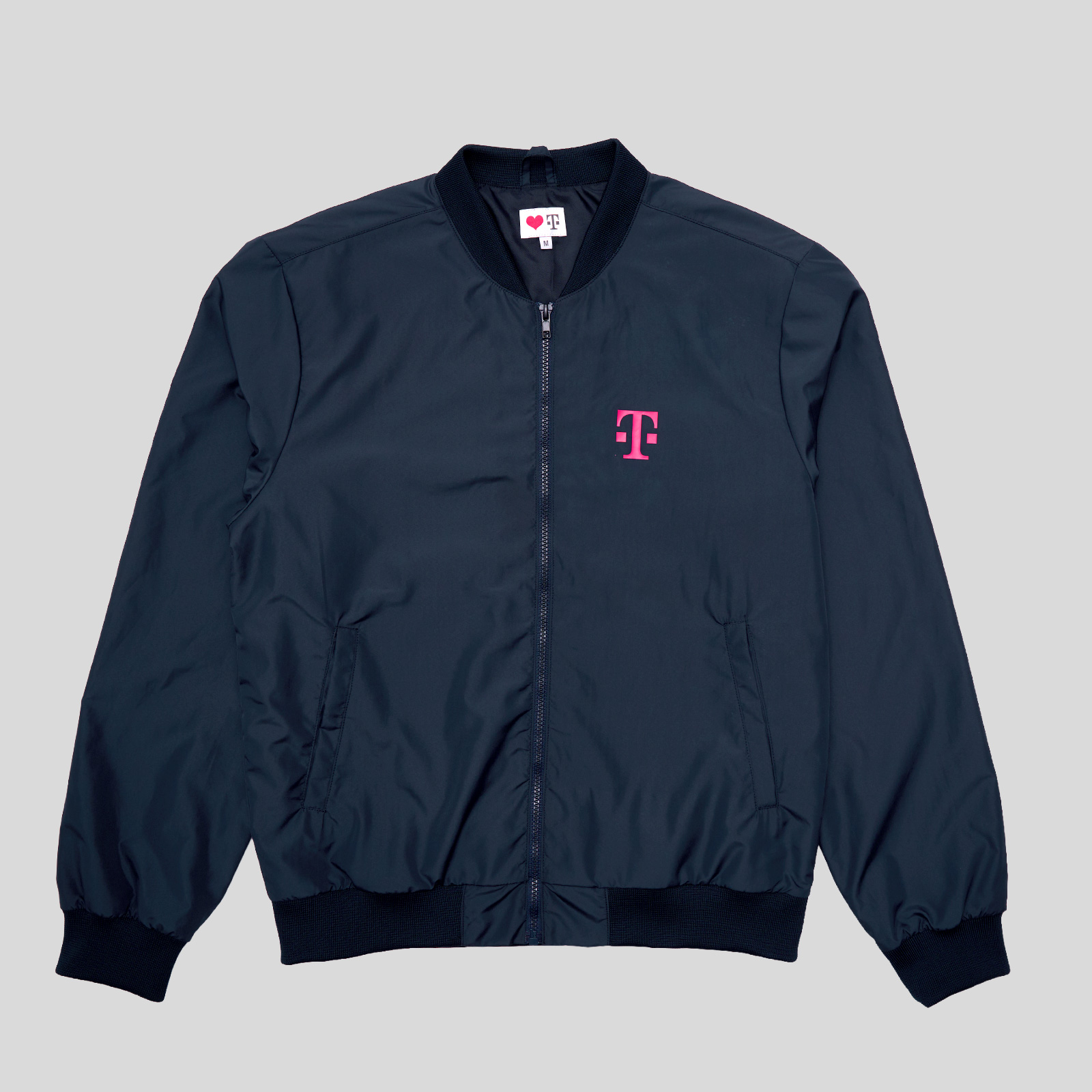 Eine marineblaue Bomberjacke mit Reißverschluss vorne und gerippten Bündchen, verziert mit einem rosa T-Logo auf der linken Brust.