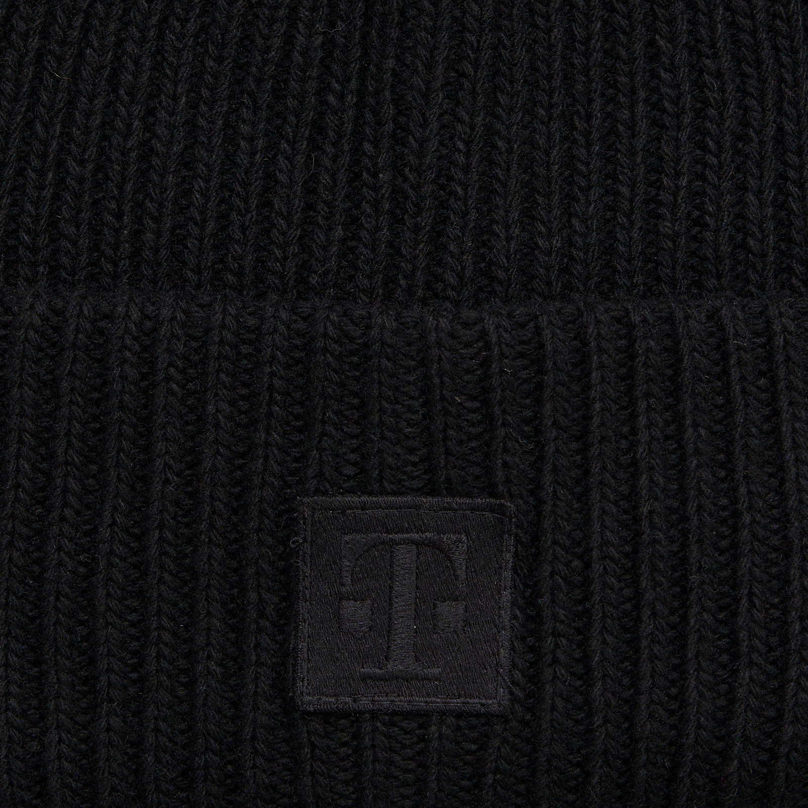 Detailansicht des breiten Umschlags der LOGO BEANIE BLACK mit gesticktem T-Logo-Patch Ton in Ton