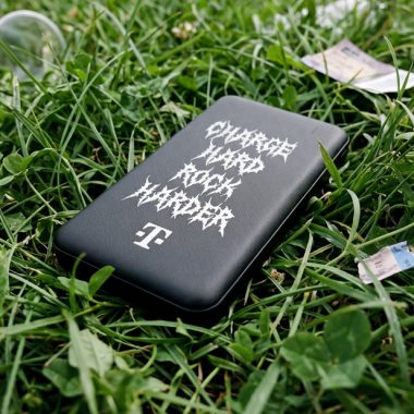 A black portable power bank featuring stylized white text and a magenta logo on green grass, surrounded by clover leaves and small decorative accents.